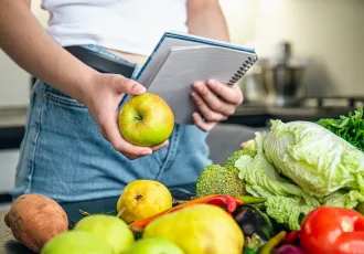 Woman with notepad and vegetables on the kitchen table, cooking a recipe, the concept of dieting, counting calories and losing weight.